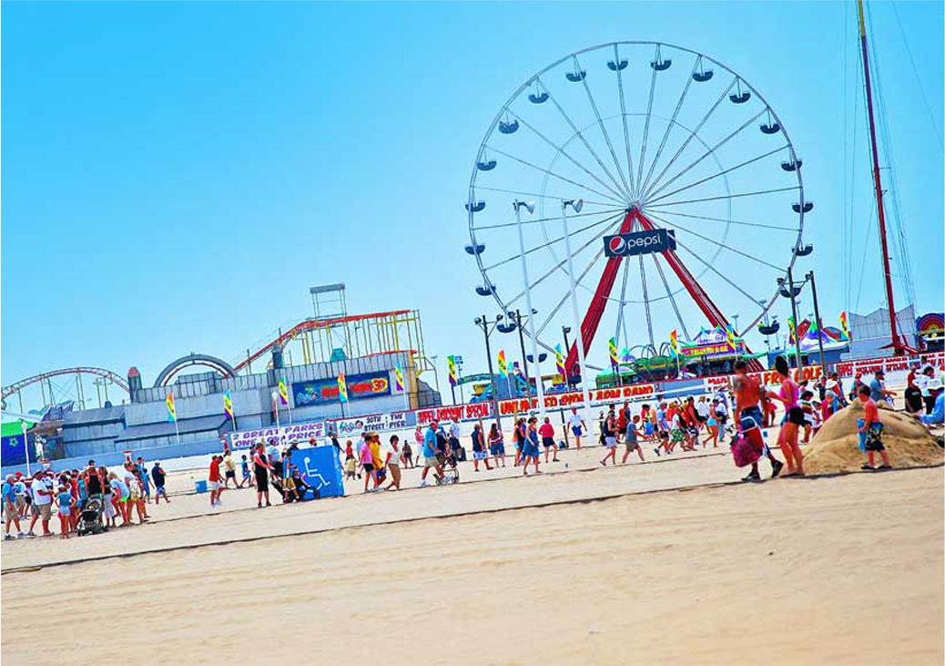 a crowd of people walking along a sandy beach next to a ferris wheel